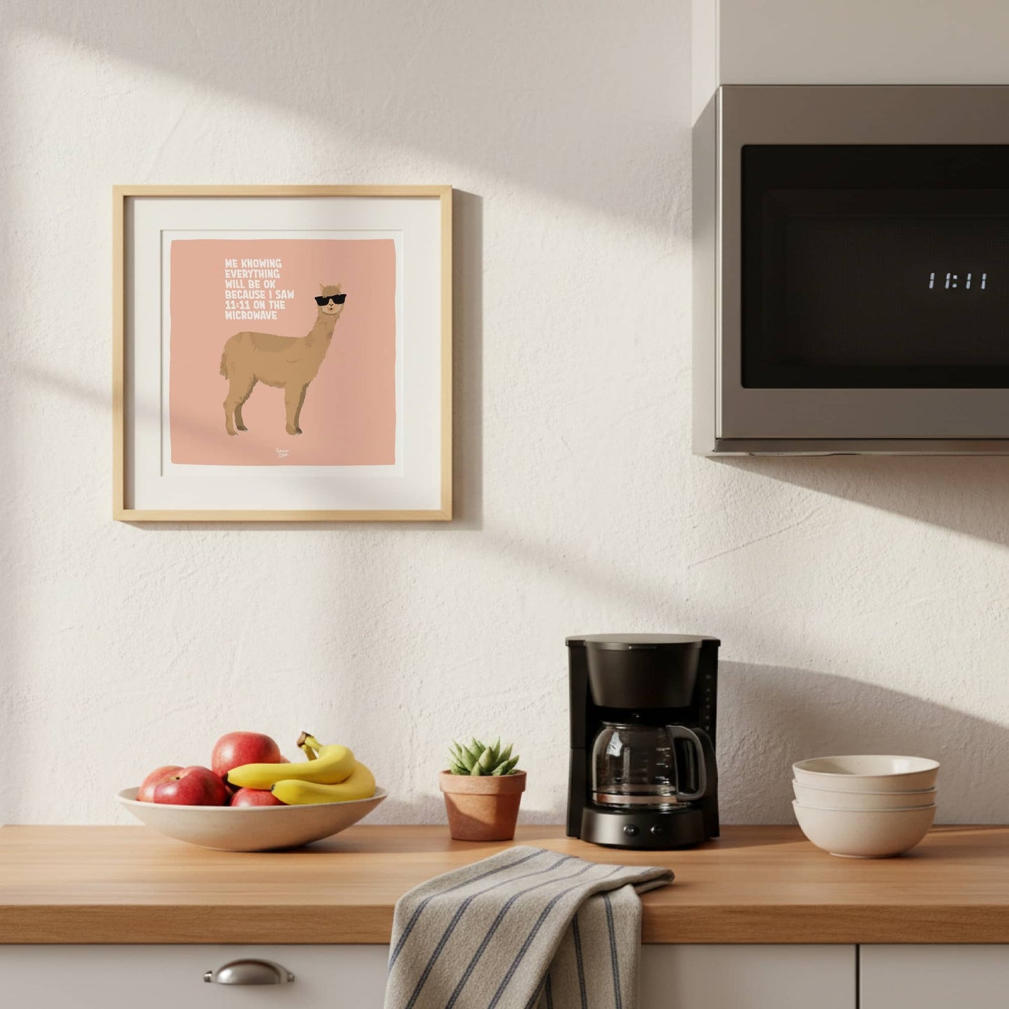The square format layout of the alpaca print with the English text, beautifully framed and hanging on a contemporary kitchen wall. This location adds an extra layer of humor right next to where the microwave action actually happens.