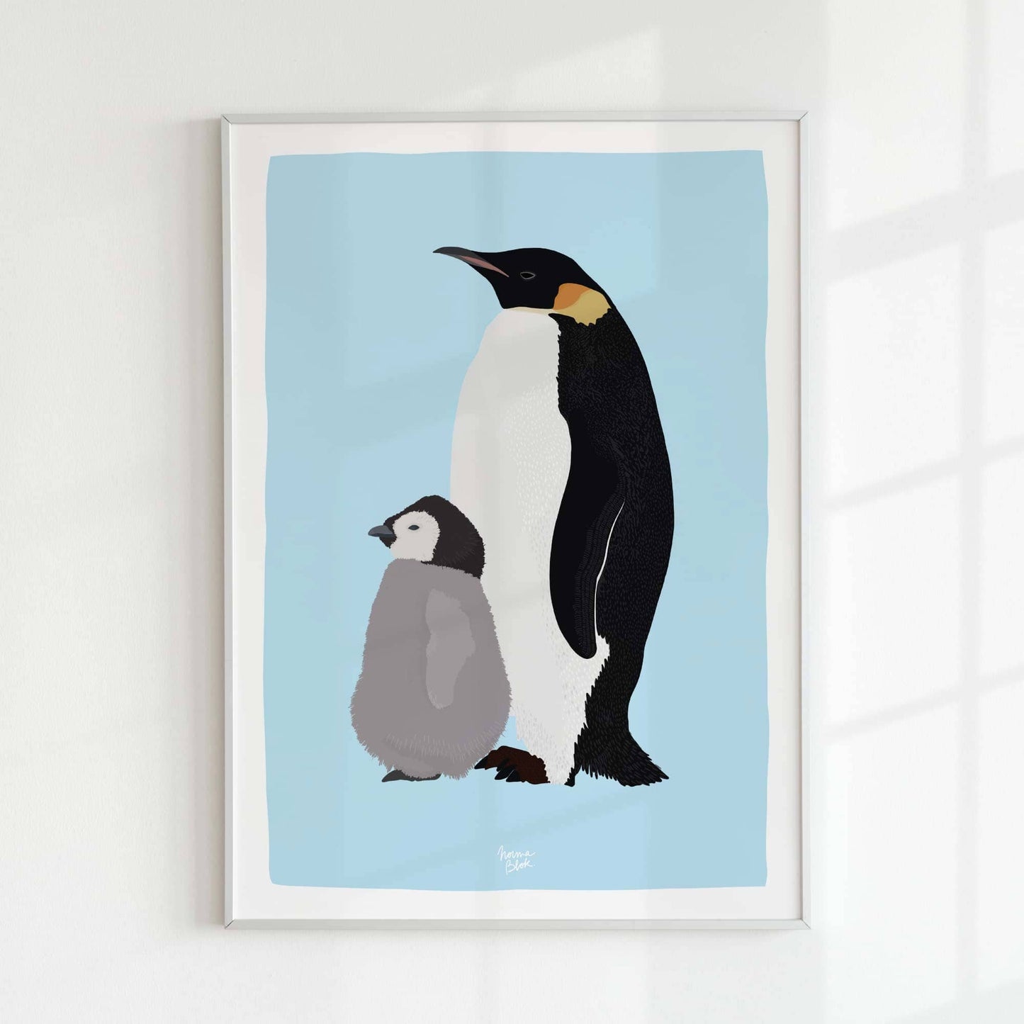 Emperor penguin print in a minimalist white frame on a white wall, illuminated by natural light from a window. Elegant home decor style.