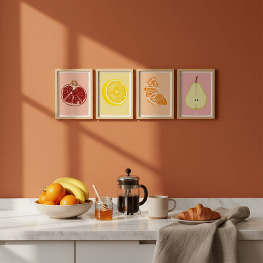 Pack de láminas de frutas en marcos de madera clara sobre una pared de cocina color teja. Muestra cómo quedan colgadas.