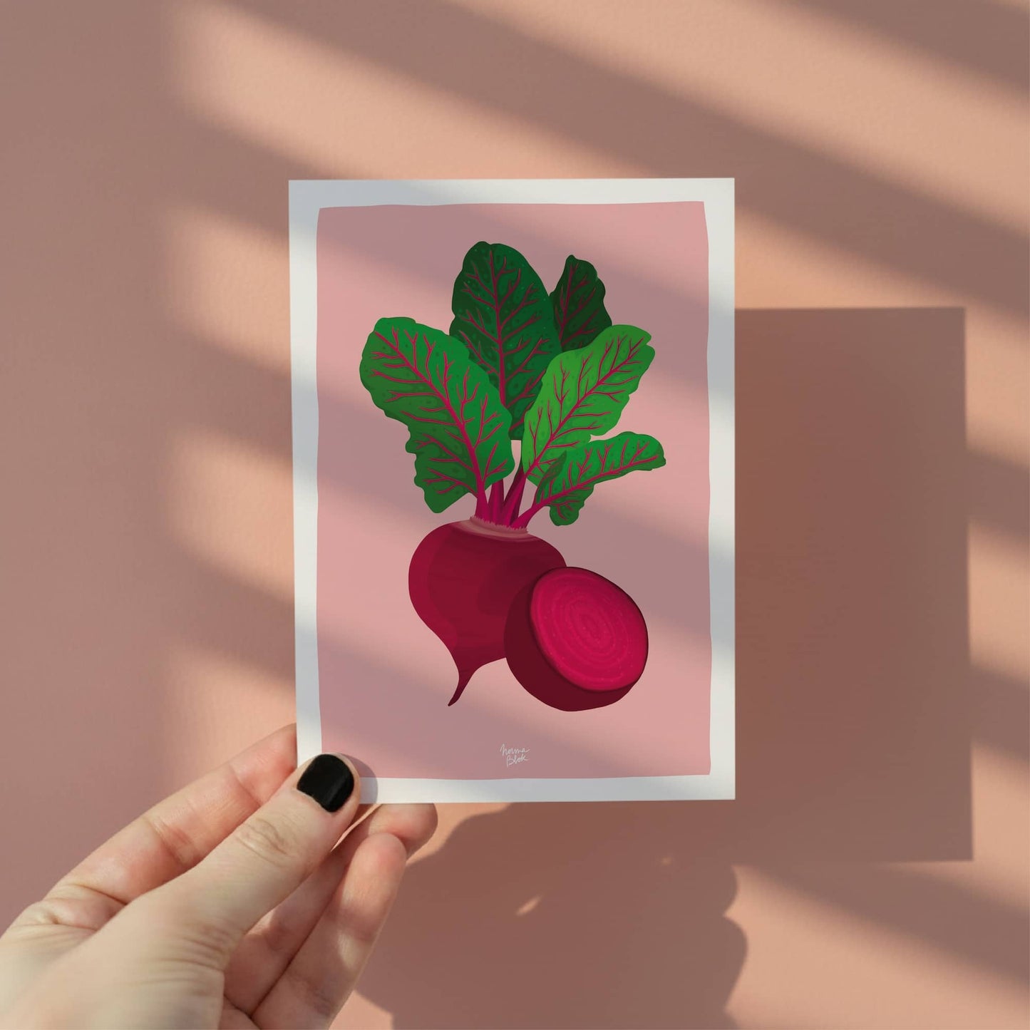 Una mano sosteniendo la mini lámina de la remolacha para mostrar el tamaño A6 y el fondo rosado vibrante, ideal para usar como ficha de receta o decoración.