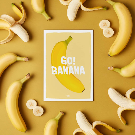The "Go Banana" postcard displayed on a colorful office desk with bananas around it, illustrating how it adds a humorous and nostalgic touch to a workspace by Normablo