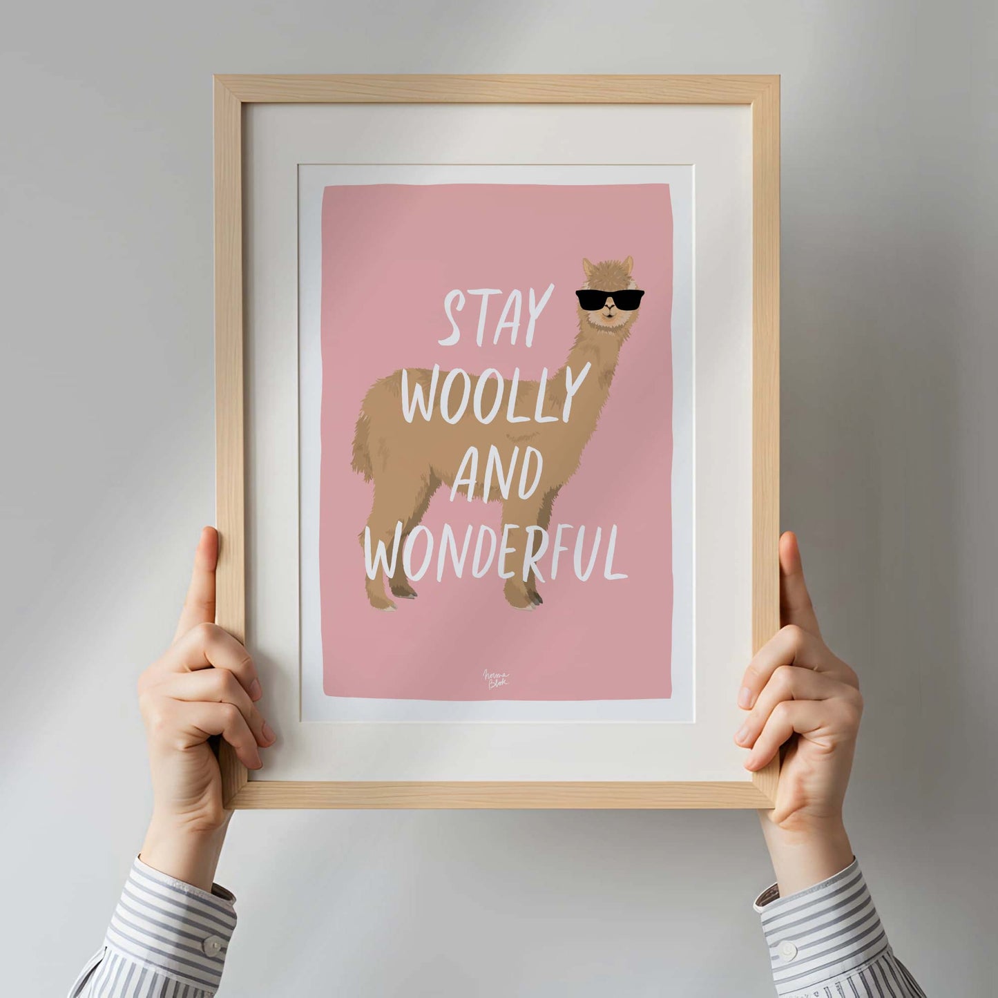 A close-up shot of a hand holding the printed alpaca illustration, providing a real-life physical reference for the scale, paper texture, and vibrant pink color finish. This perspective helps customers visualize the artwork size before hanging it up.