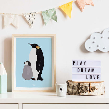 Emperor penguin art print in a frame, leaning on a white dresser in a modern nursery. A clean and cozy children's room decoration idea.