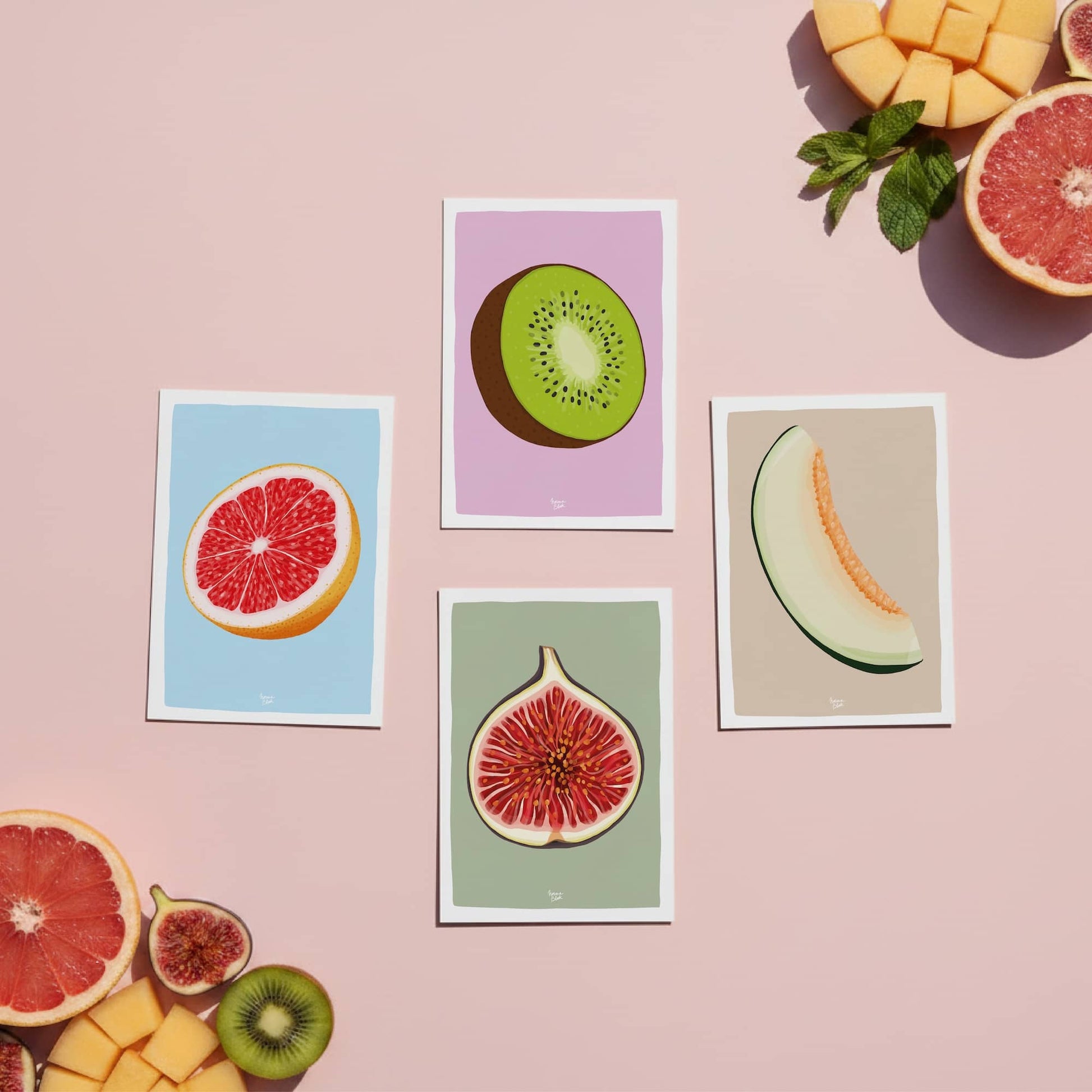 A collection of four fruit-themed mini prints—higo, kiwi, melón, and pomelo—displayed on a soft pink background surrounded by real fruit. These colorful, modern illustrations are part of a collection for curious minds who appreciate the small details in everyday objects. By normablok.