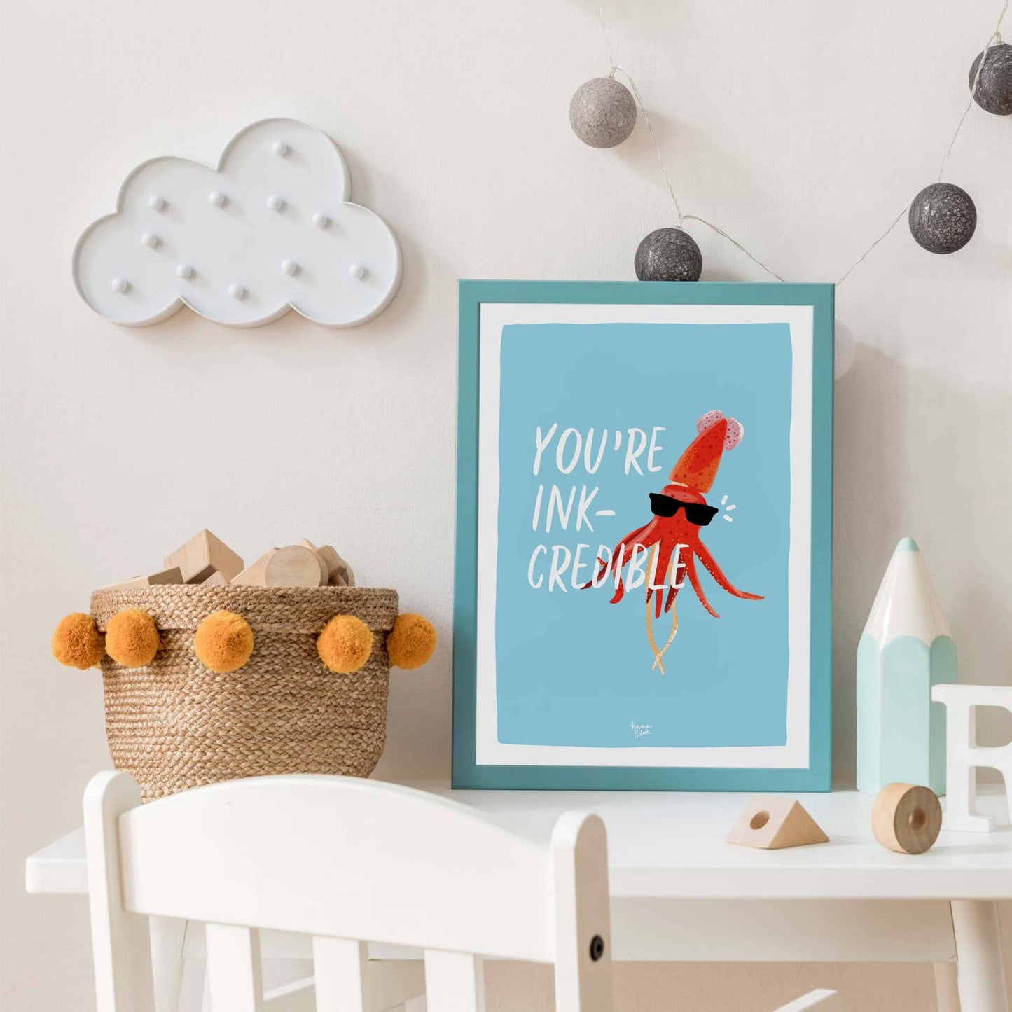 An A4 size squid print inside a solid, bright blue frame hanging on the wall of a contemporary kids' bedroom. The colorful framing complements the playful artwork, showing how a simple illustration can add character to a children's playroom or sleeping area.