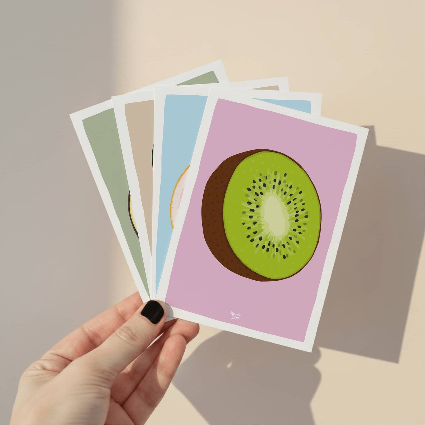 Una mano sosteniendo el pack de láminas de frutas para mostrar el tamaño A6 y la calidad del diseño digital figurativo de Normablok.