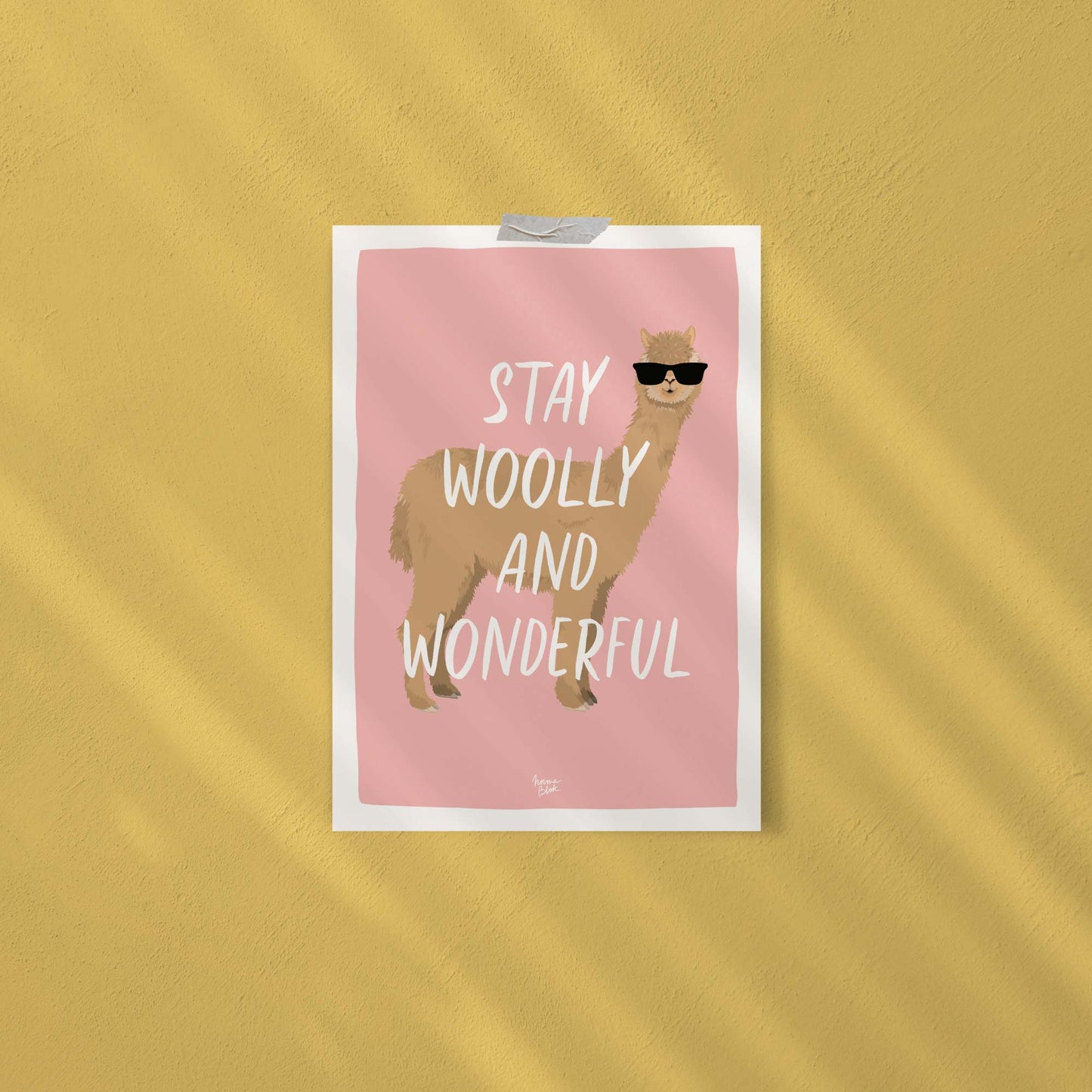 The funny alpaca digital illustration with sunglasses attached directly to a studio wall using decorative pieces of washi tape. This display shows an easy, casual, and framework-free way to decorate a small knitting workshop or home workspace with style.