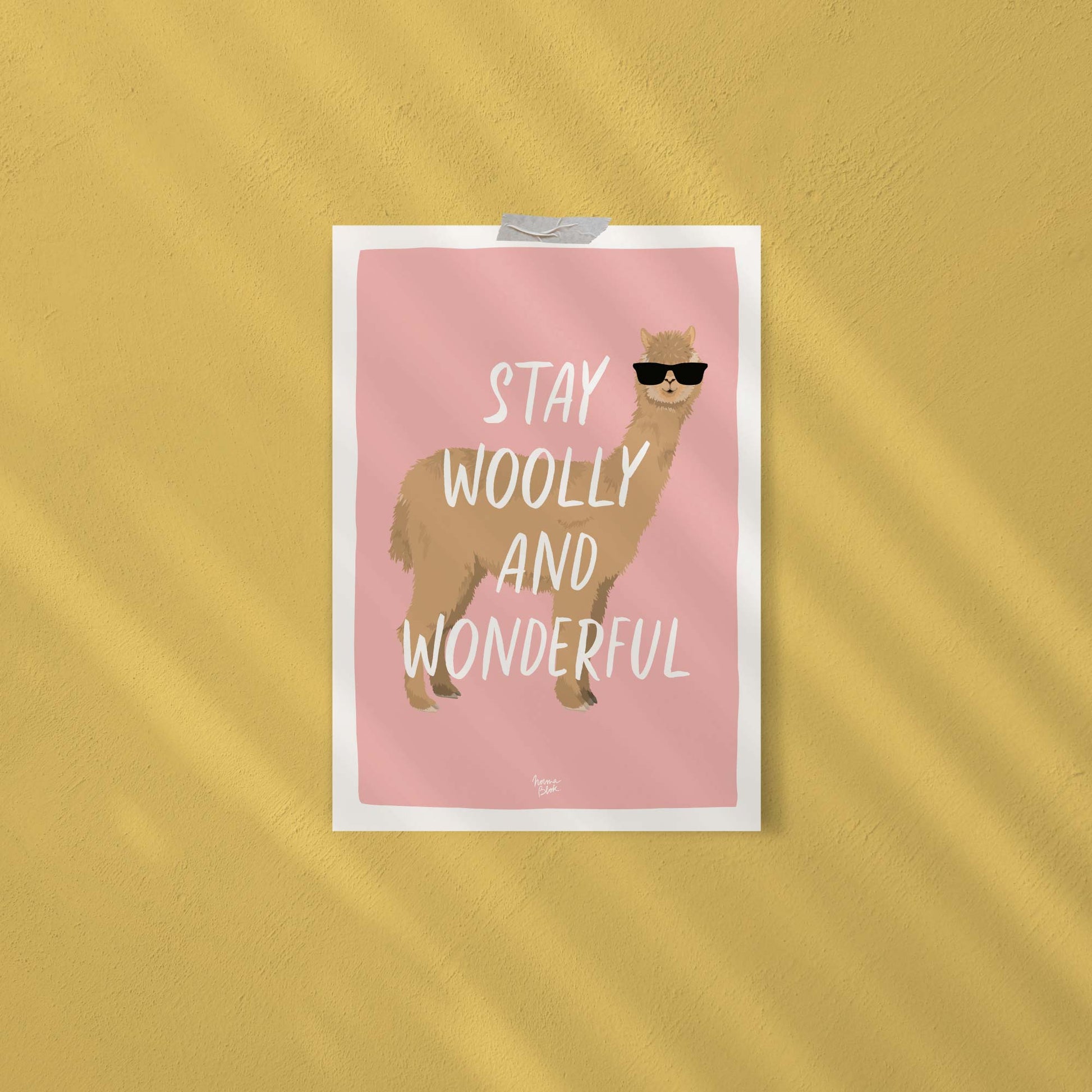 The funny alpaca digital illustration with sunglasses attached directly to a studio wall using decorative pieces of washi tape. This display shows an easy, casual, and framework-free way to decorate a small knitting workshop or home workspace with style.
