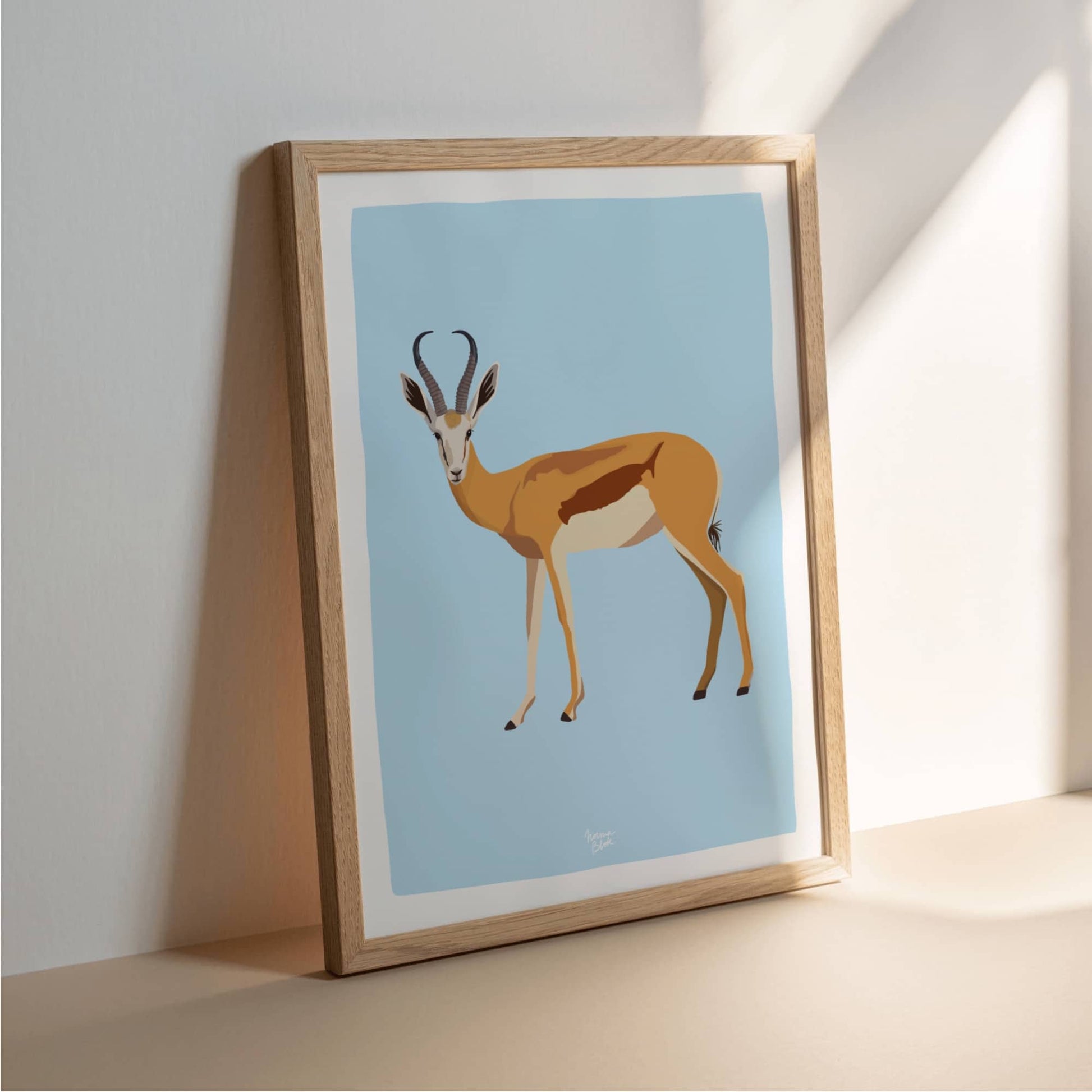 An antelope art print in a clean, light wood frame, stylishly leaning against a minimalist white wall. This interior decor scene emphasizes a Scandinavian-inspired aesthetic, perfect for those looking for airy and modern home styling.