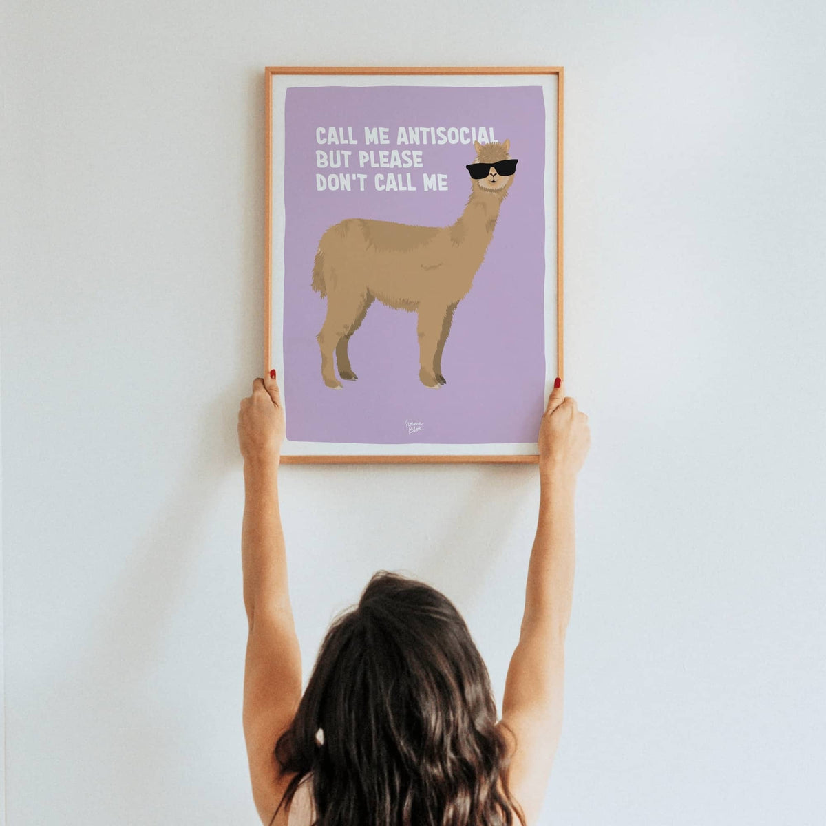 A lifestyle shot of a woman holding up a framed A3 size alpaca art print in a real room by Normablok.
