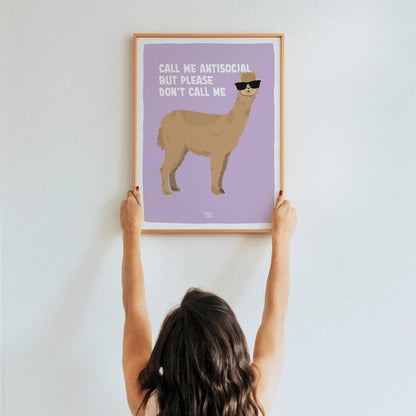A lifestyle shot of a woman holding up a framed A3 size alpaca art print in a real room by Normablok.