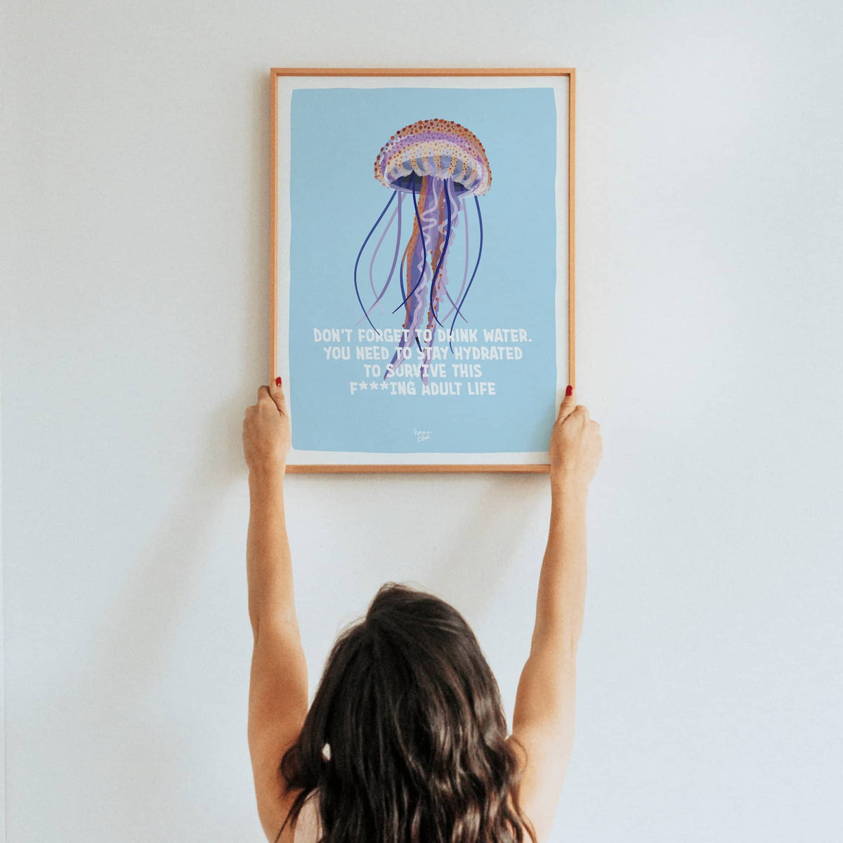 A lifestyle shot of a woman holding up a framed A3 size print to showcase its scale and visual impact in a real space.