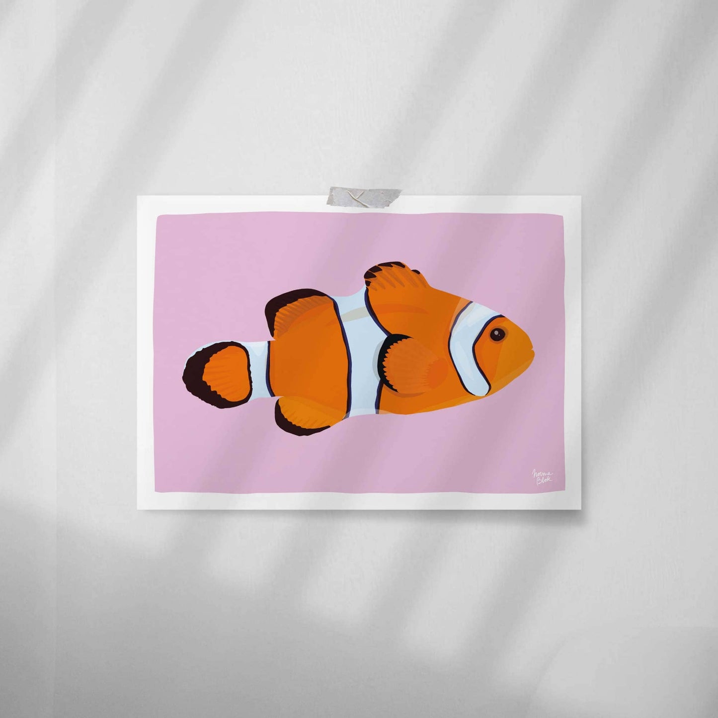 Vista en primer plano de la lámina del pez payaso pegada en una pared blanca lisa con celo. Este estilo minimalista muestra la textura de la impresión y cómo decorar un espacio sin usar marco.