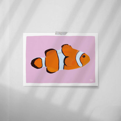 Vista en primer plano de la lámina del pez payaso pegada en una pared blanca lisa con celo. Este estilo minimalista muestra la textura de la impresión y cómo decorar un espacio sin usar marco.