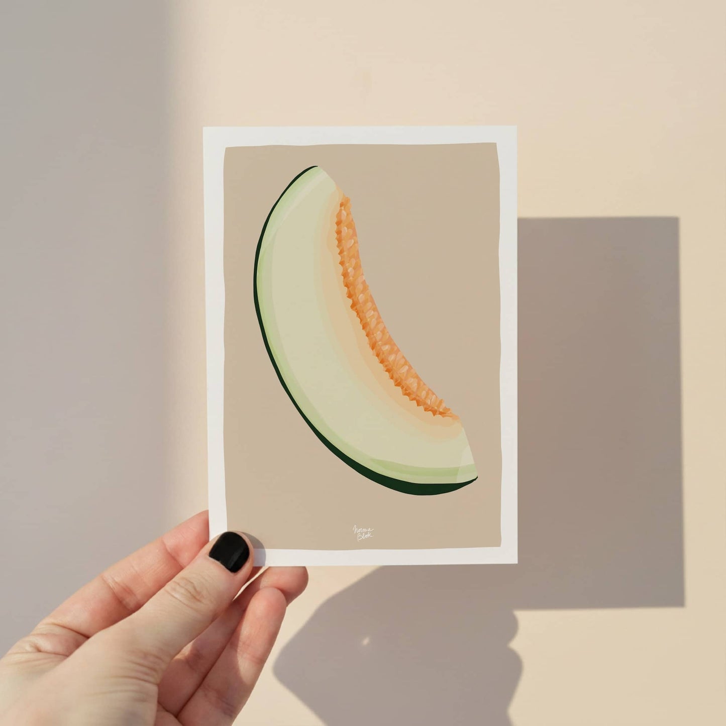 A close-up shot of a hand holding the melon mini print, showcasing the detailed figurative design and the signature white border. The soft beige background highlights the vibrant colors of this A6 digital illustration, perfect for use as a bookmark or small wall art. By normablok.