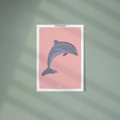 The pink dolphin art print casually attached to a soft celadon green wall using clear tape on the corners. The contrast between the soft pink illustration and the serene green wall creates a modern, calming, and stylish aesthetic for a kid's bedroom.