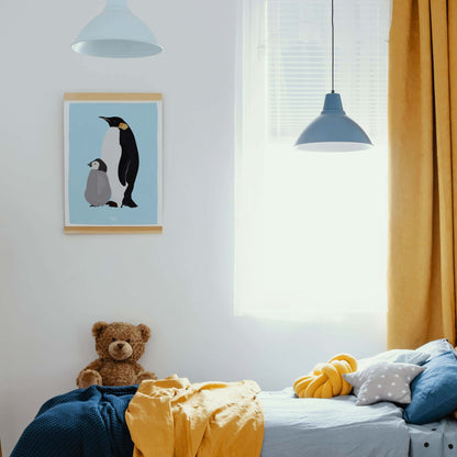 Emperor penguin print hanging with a magnetic wooden frame in a kids' room with blue and yellow bedding and a plush bear toy.
