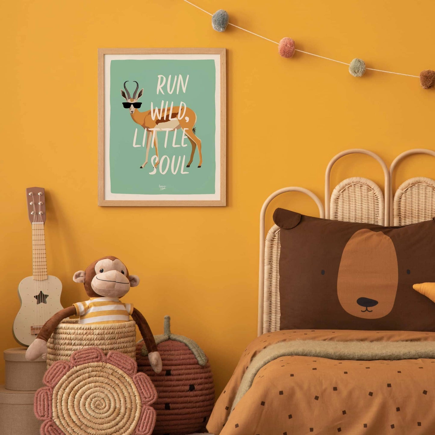 The turquoise antelope art print in a modern frame on a vibrant mustard yellow wall in a kids' bedroom. The scene includes a plush monkey toy and a cute bear-shaped cushion on a bed, showing how the bold color contrast creates a fun, modern, and stylized children's space.