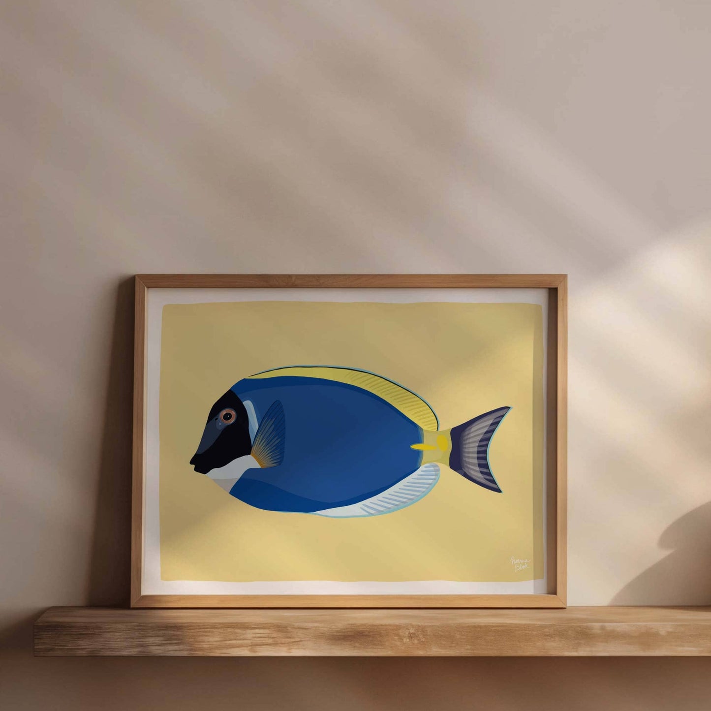 Blue Tang fish art print in a natural wood frame, resting on a rustic wooden floating shelf. A cozy and simple home decor idea.
