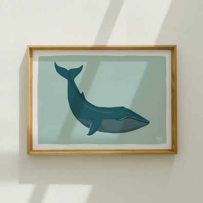 The blue whale art print displayed in a beautiful wooden frame on a clean white wall. Natural light streams in from windows, creating a cozy and inviting atmosphere and highlighting how well this piece fits a relaxed, modern aesthetic.