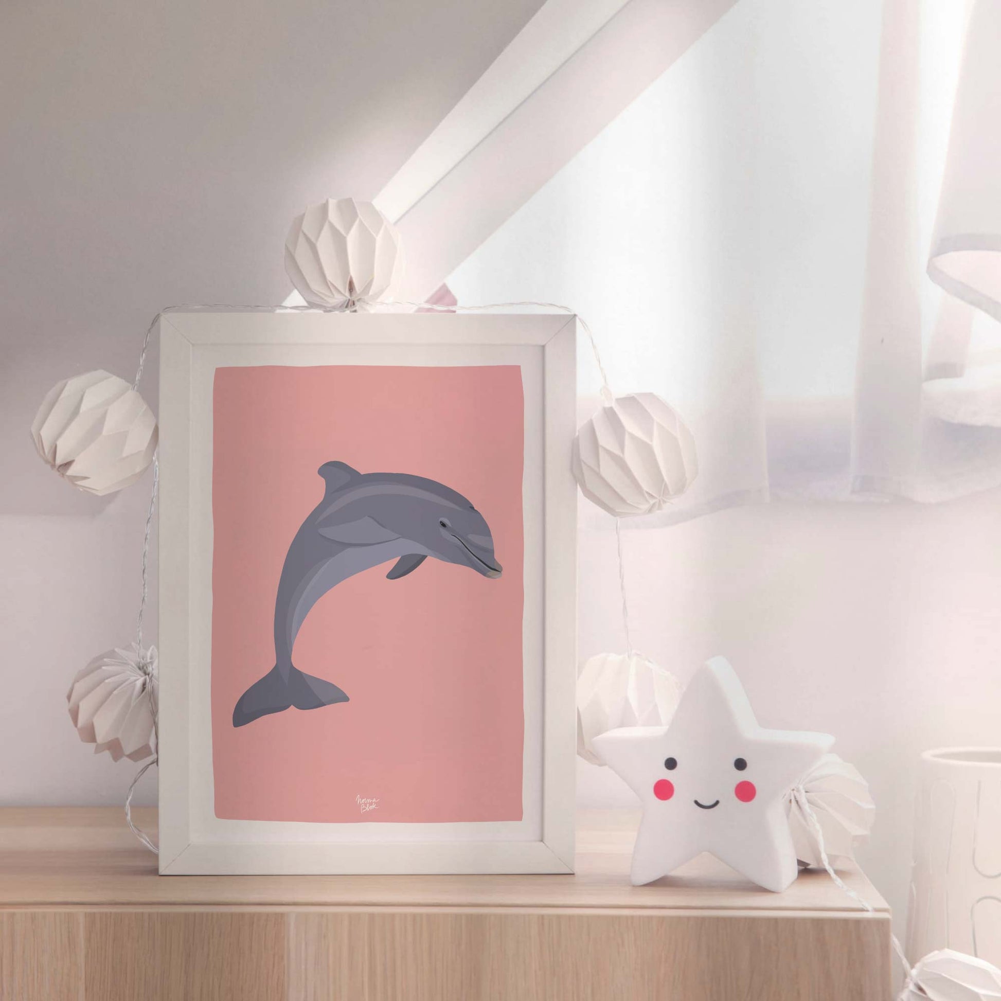 Framed dolphin print in an elegant white molding frame, leaning on a wooden dresser in a nursery next to a glowing star-shaped night light. This cozy setup creates a soft, dreamy environment perfect for bedtime and early childhood decor.