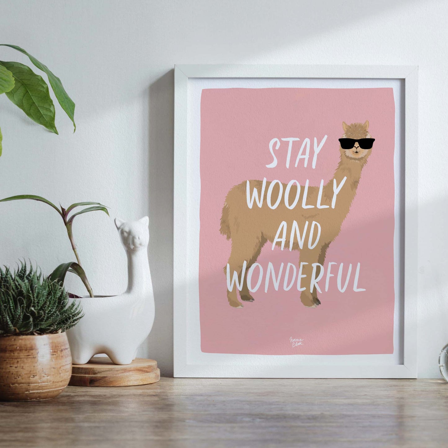 The alpaca art print in a modern frame, styled inside a creative craft room. It sits on a shelf surrounded by colorful yarn balls, knitting needles, and textile tools, showing how this humorous print adds personality and a modern touch to a dedicated sewing space.