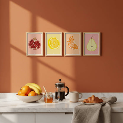 Pack de láminas de frutas en marcos de madera clara sobre una pared de cocina color teja. Muestra cómo quedan colgadas.
