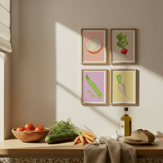 The four vegetable prints in wooden frames sitting on a kitchen counter next to a fresh tomato, carrots, and zucchini, showing how they look as professional kitchen decor.