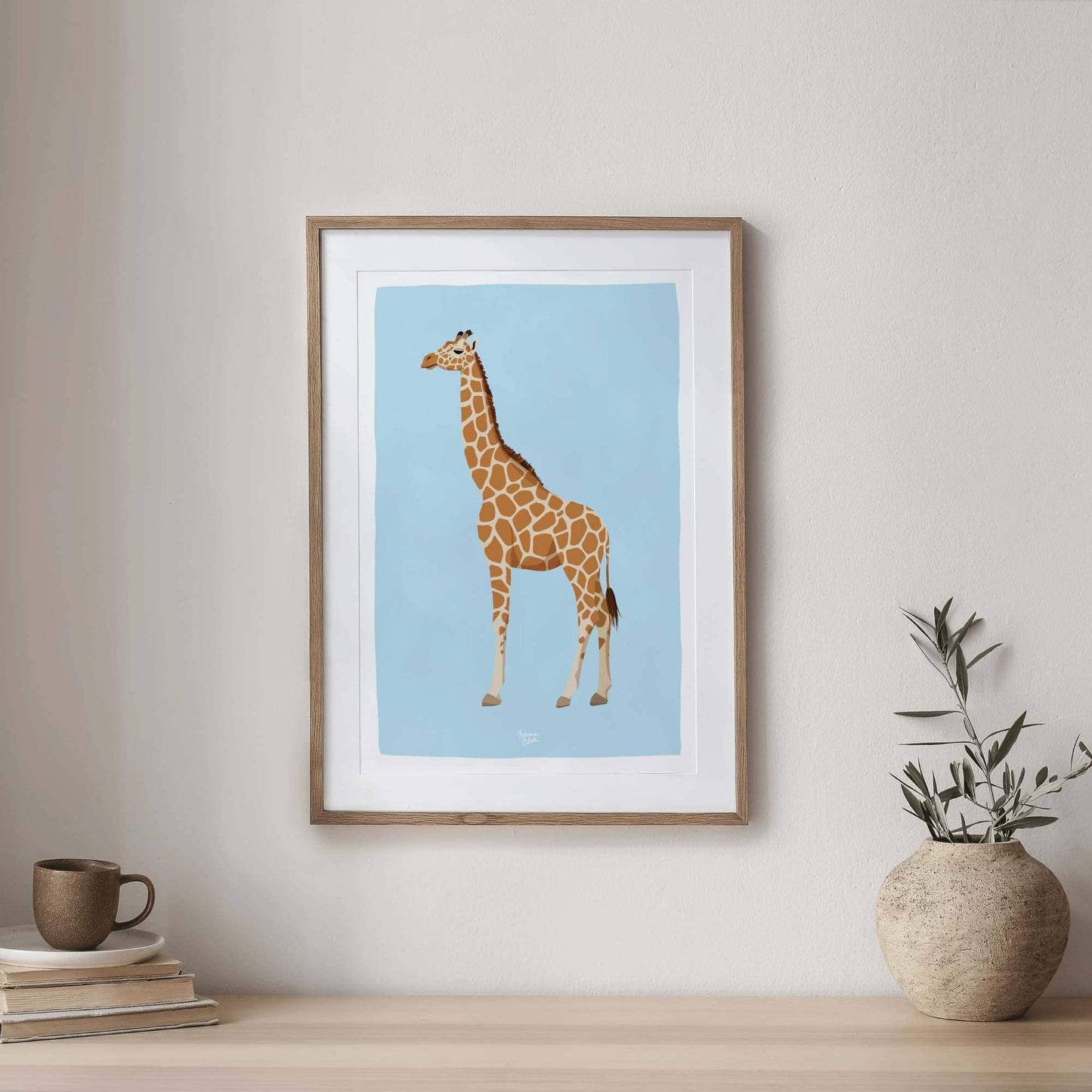 Giraffe illustration showcased in a sophisticated dark wood frame on an entryway console. Styled with a green plant and books, this home styling demonstrates how professional wildlife wall art elevates the elegance and design of your home entrance.
