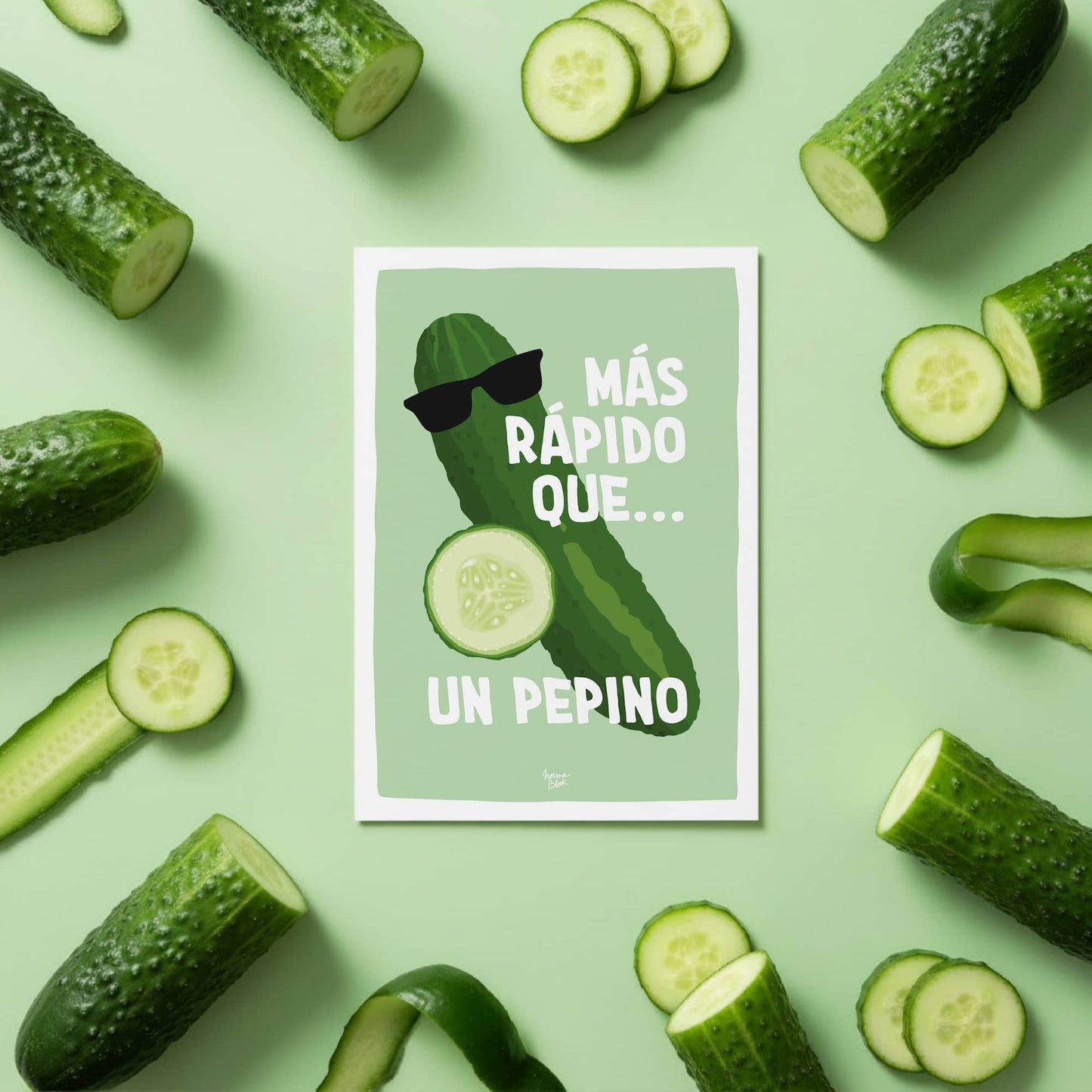 Vista cenital de la mini lámina "más rápido que un pepino" colocada en el centro de una mesa y rodeada de pepinos reales, destacando el divertido detalle de las gafas de sol en el diseño ilustrado por normablok.