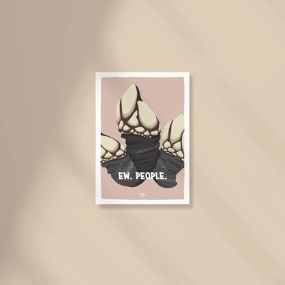 A cozy work-from-home desk setup with a framed "Ew. People." barnacle mini print sitting next to a laptop, a coffee mug, and a small potted plant by Normablok.