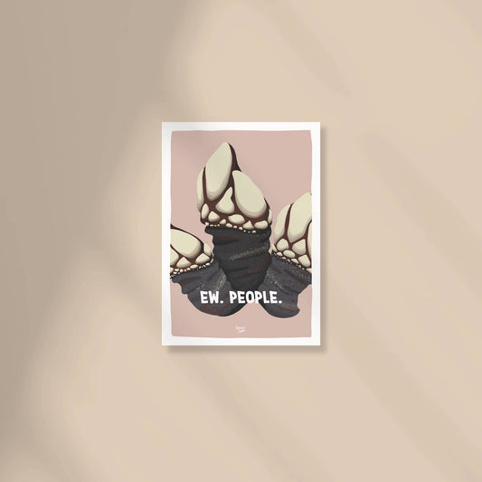 A cozy work-from-home desk setup with a framed "Ew. People." barnacle mini print sitting next to a laptop, a coffee mug, and a small potted plant by Normablok.