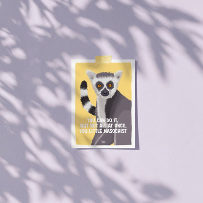 An A6 mini art print featuring the hilarious "You can do it. But not all at once, you little masochist." lemur illustration taped casually to a wall using colorful patterned washitape. The image highlights how quick and easy it is to hang or display this unframed postcard on a home office wall, workspace, or bedroom cubicle without damaging the paper or wall by Normablok.