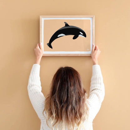 A woman holding an unframed A4-sized orca print, showing the paper quality and the sharpness of the digital illustration for wall decor.