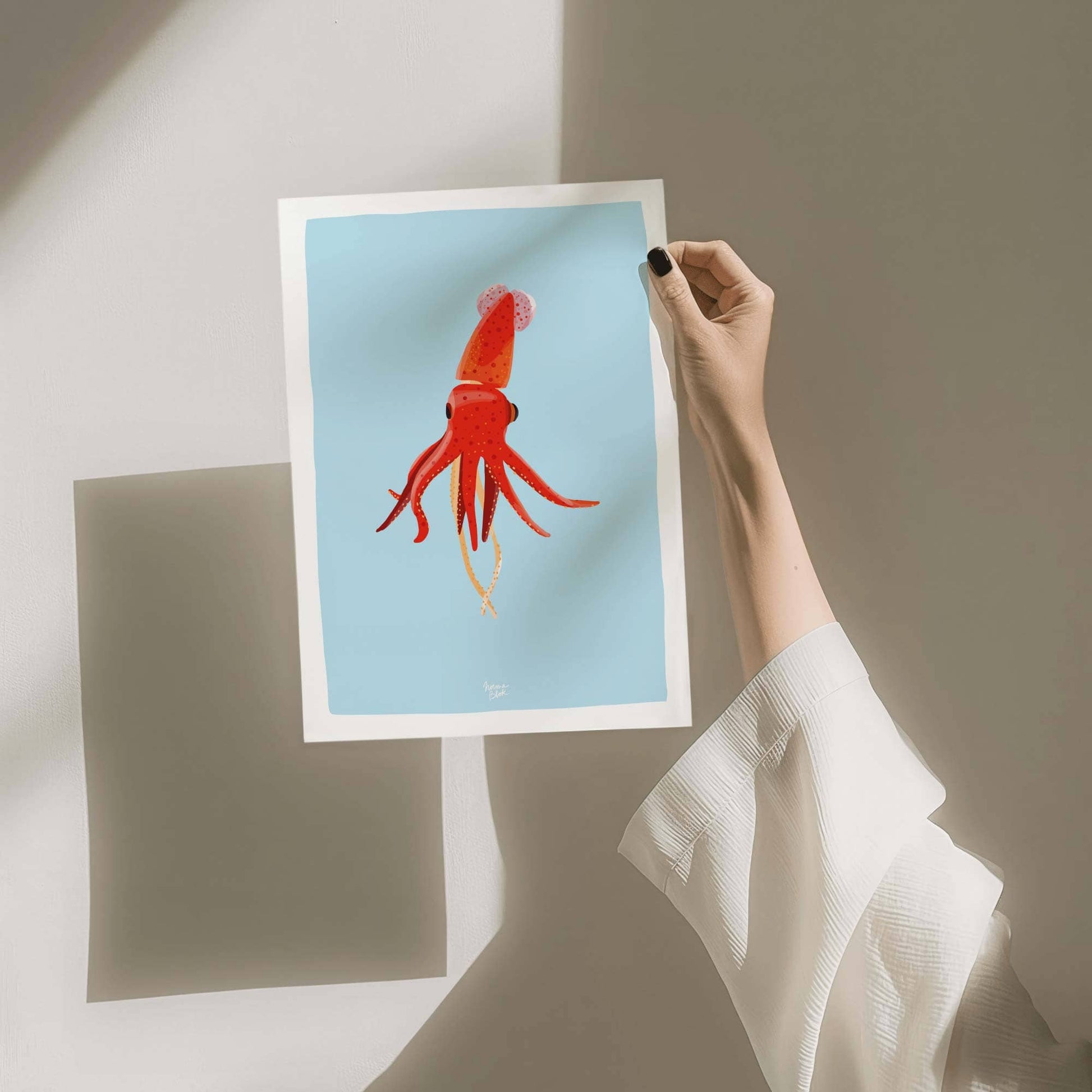 A hand holding an unframed A4-sized squid art print, showing the paper quality and the scale of the illustration for home wall decor.