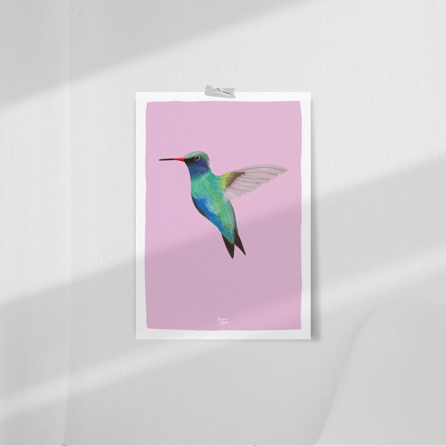 The colorful hummingbird art print casually attached to a clean white wall using simple clear tape on the corners. This simple styling highlights the violet background and vibrant bird illustration, perfect for a modern, minimalist nursery setup.