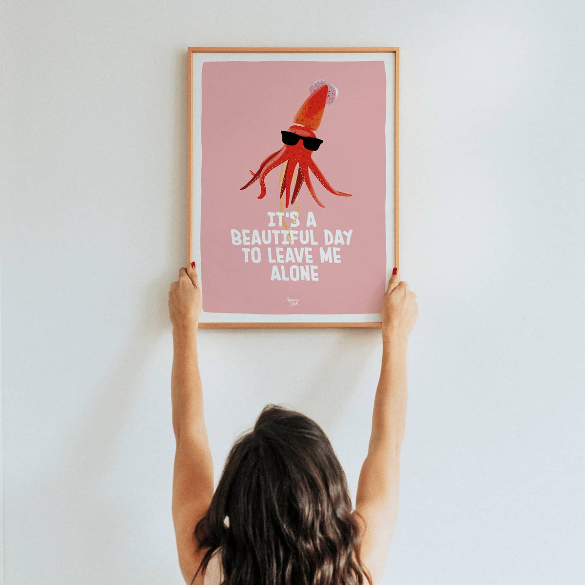 A lifestyle shot of a woman holding up a framed A3 size squid art print in a real room by Normablok.