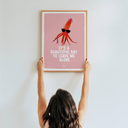 A lifestyle shot of a woman holding up a framed A3 size squid art print in a real room by Normablok.