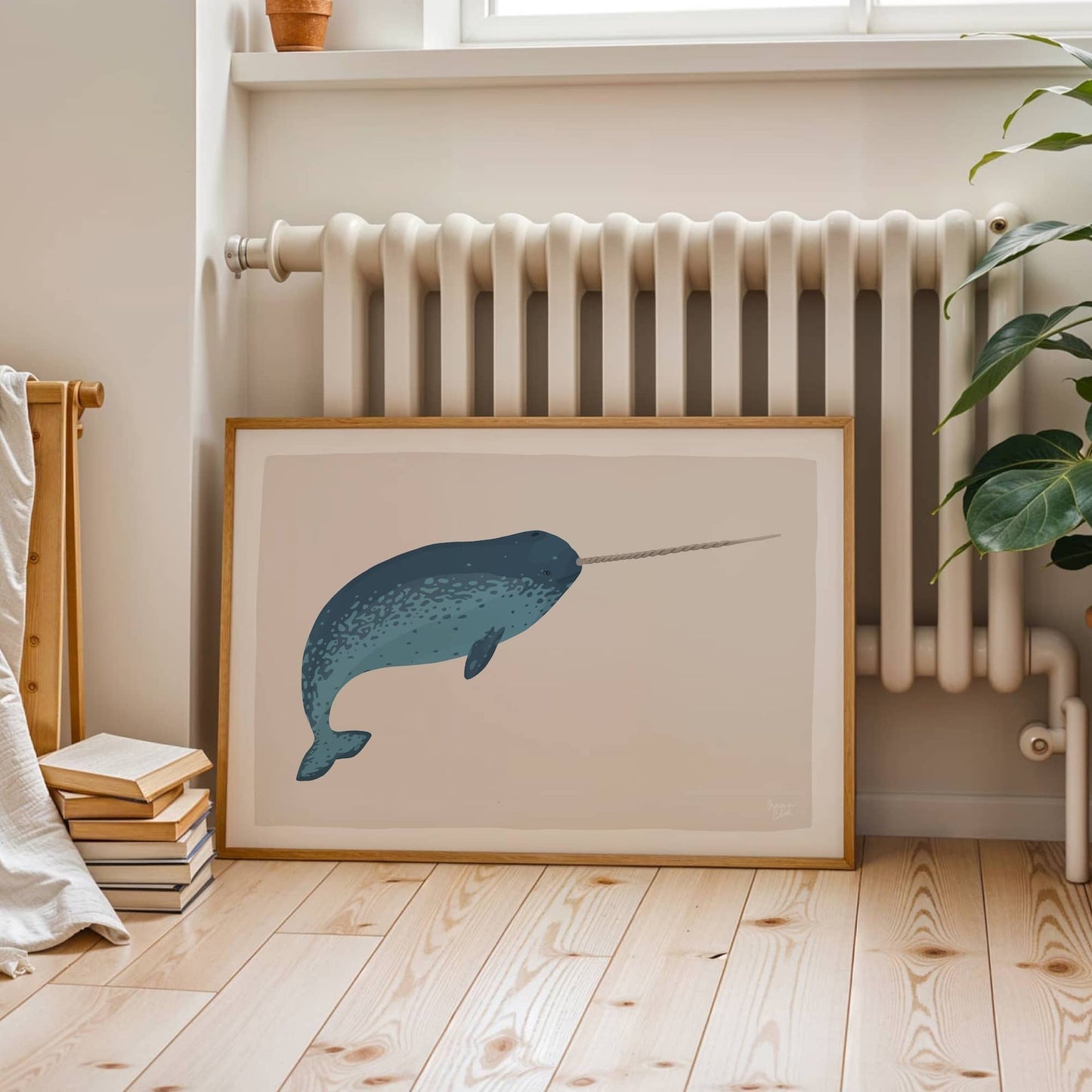 A large narwhal art print leaning against a wall in a room, positioned near a radiator, showing how to style art in a cozy, lived-in space.