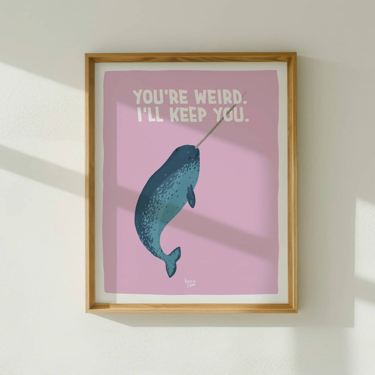 The quirky narwhal art print framed in light wood, hanging on a white wall with natural window light by Normablok.