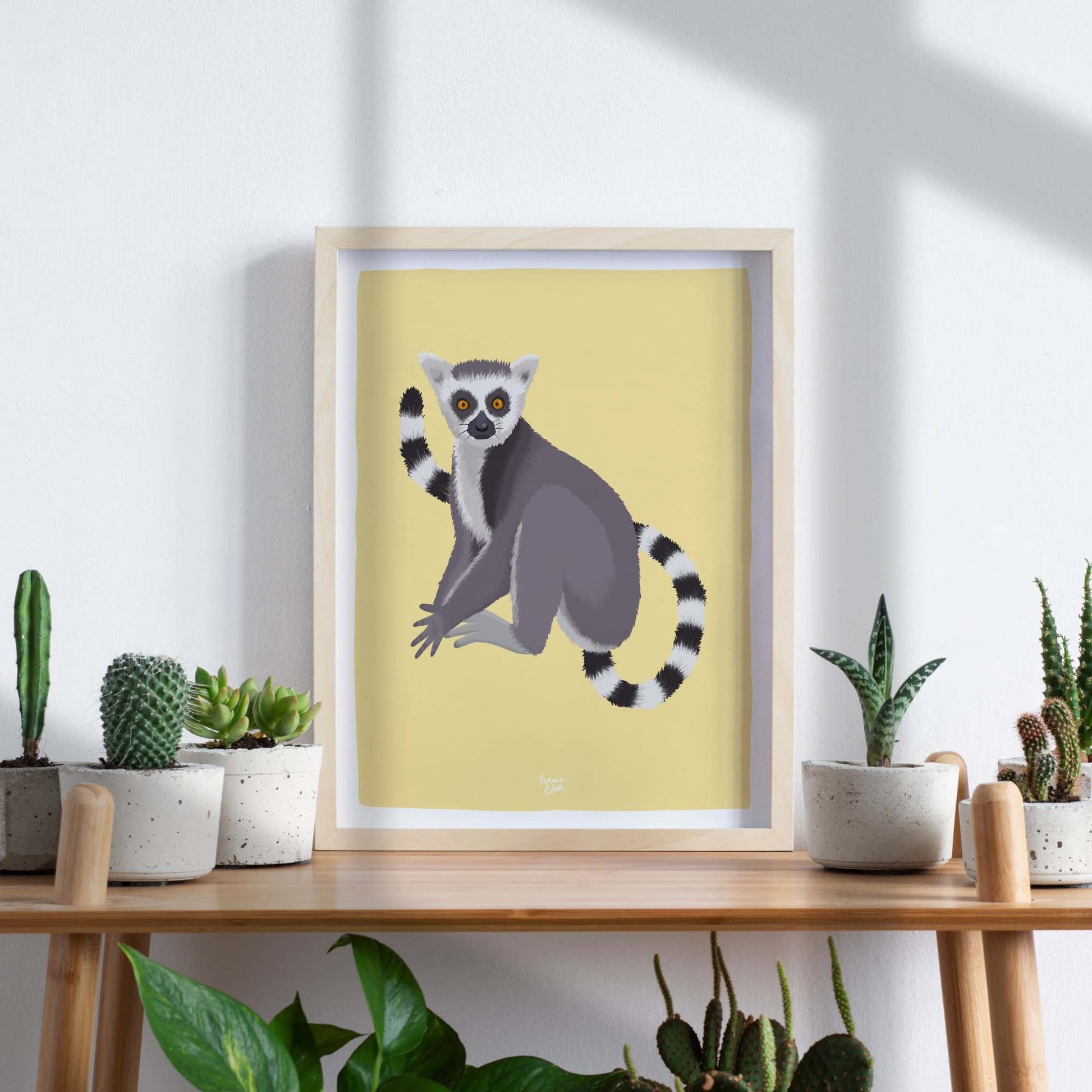 A framed lemur art print styled on a wooden table surrounded by several lush green houseplants. This interior scene shows how blending nature-inspired wildlife art with real botanical elements creates a cozy, fresh, and vibrant atmosphere in your home decor.