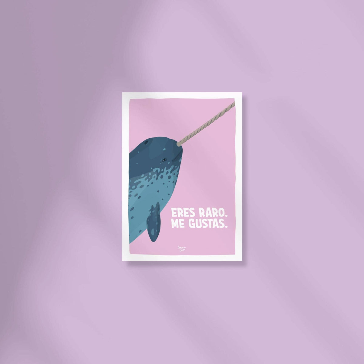 Mini lámina A6 de la cabecita de un narval sobre fondo lila claro con la frase "eres raro, me gustas" encima de una superficie de color.