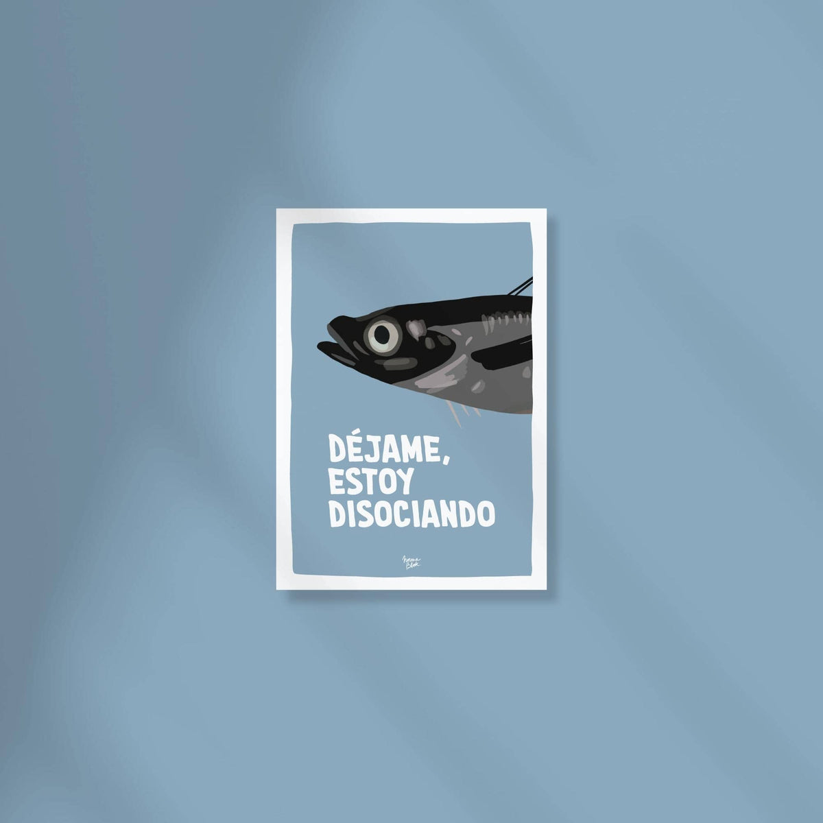 Mini lámina A6 de una sardina gris sobre fondo azul marino con la frase "déjame, estoy disociando" encima de una superficie de color.