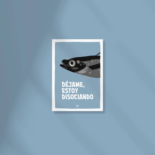 Mini lámina A6 de una sardina gris sobre fondo azul marino con la frase "déjame, estoy disociando" encima de una superficie de color.