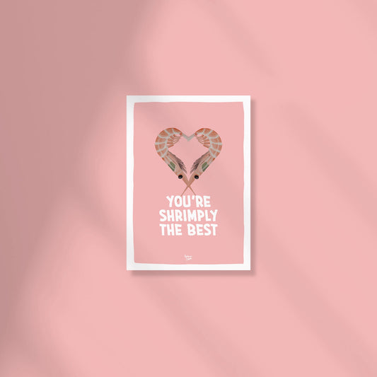 A soft pale pink A6 postcard featuring a digital illustration of two orange and red shrimps curved toward each other to form a heart shape, with the text "you're shrimply the best" written in a modern, playful font by normablok.