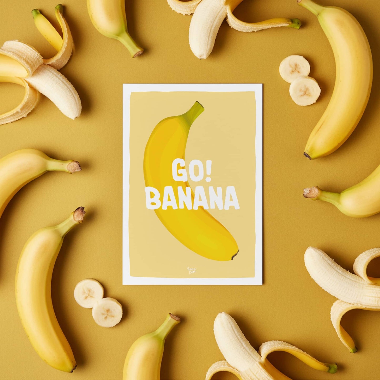 The "Go Banana" postcard displayed on a colorful office desk with bananas around it, illustrating how it adds a humorous and nostalgic touch to a workspace by Normablo