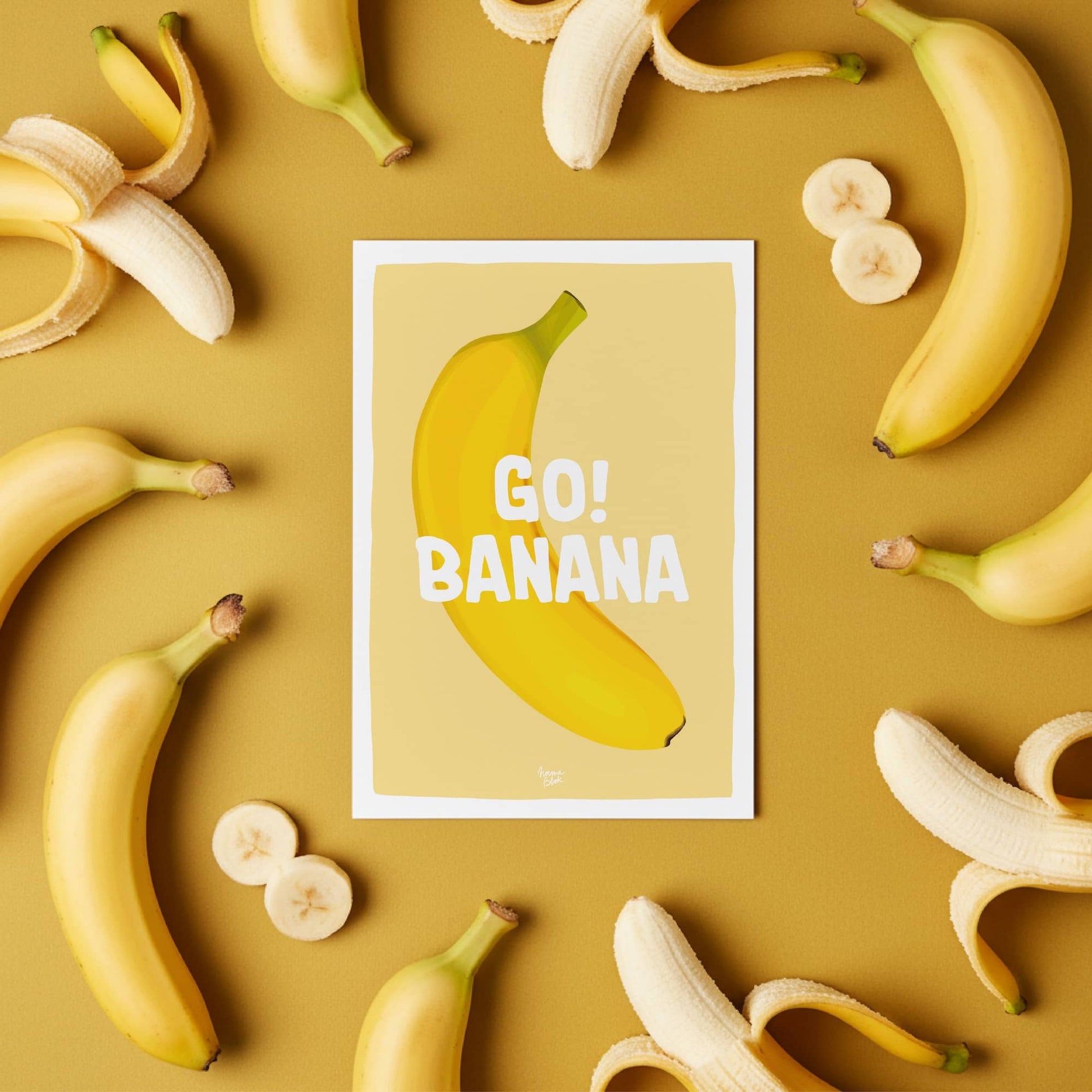 The "Go Banana" postcard displayed on a colorful office desk with bananas around it, illustrating how it adds a humorous and nostalgic touch to a workspace by Normablo