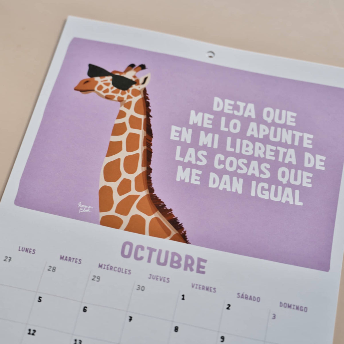 Página de octubre del calendario 2027 de Normablok con una jirafa con gafas de sol y la frase deja que me lo apunte en mi libreta de las cosas que me dan igual.