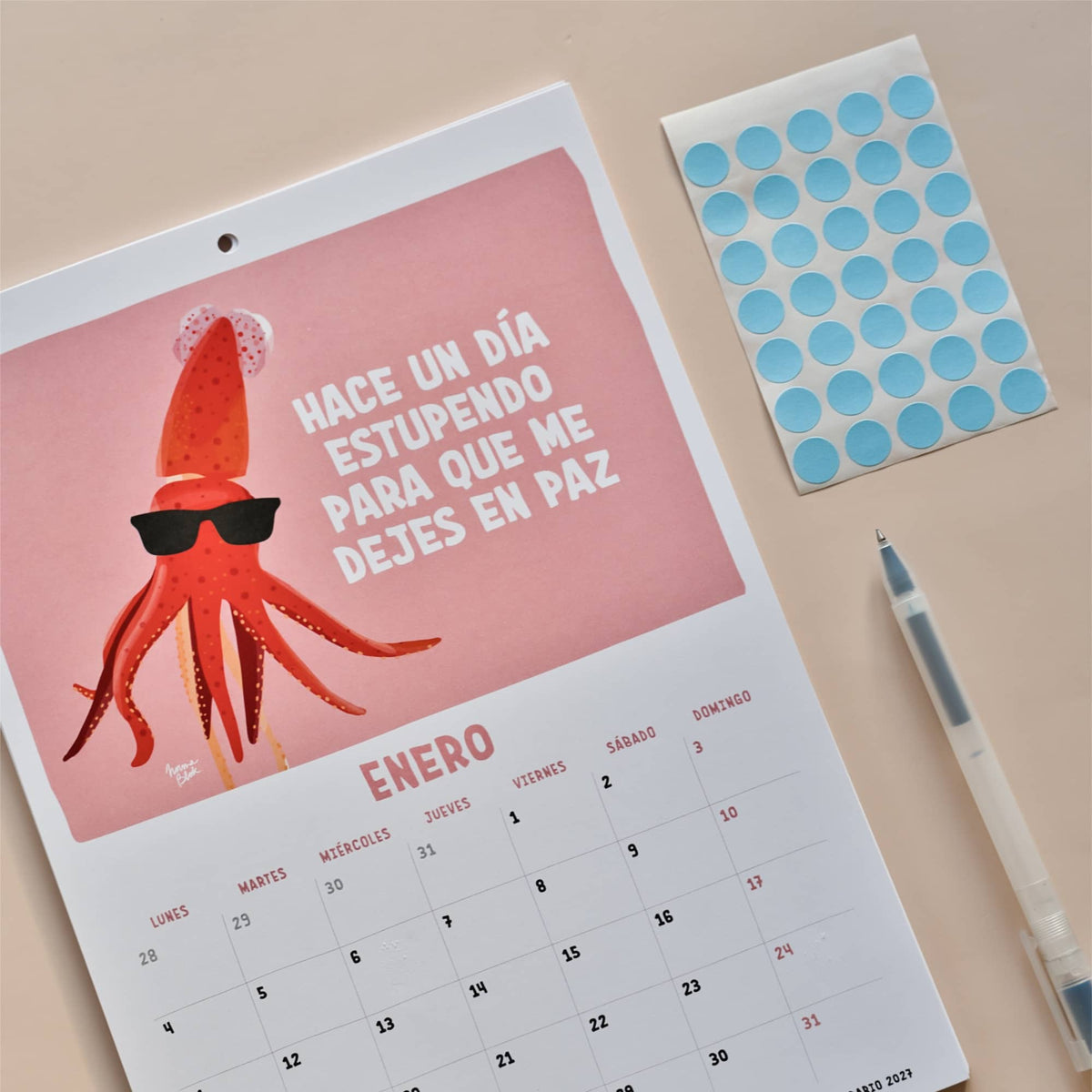 Página de enero del calendario 2027 de Normablok con un calamar con gafas de sol y la frase hace un día estupendo para que me dejes en paz. El calendario incluye pegatinas redondas para marcar festivos y fechas señaladas.