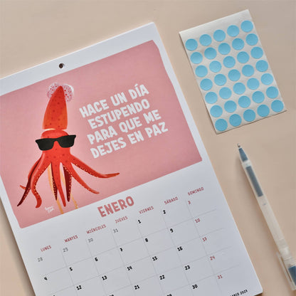 Página de enero del calendario 2027 de Normablok con un calamar con gafas de sol y la frase hace un día estupendo para que me dejes en paz. El calendario incluye pegatinas redondas para marcar festivos y fechas señaladas.